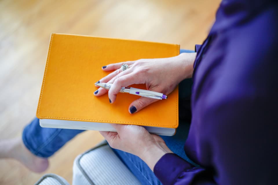 Hand mit Stift auf einem gelben Notizbuch