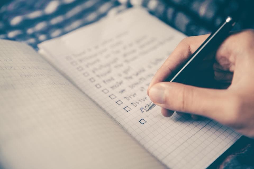 Hand hakt Kästchen auf einer Checkliste in einem Notizbuch ab