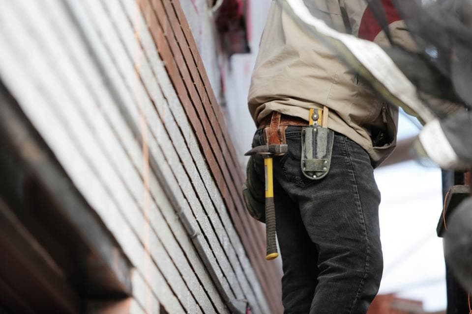 Ein Handwerker mit Werkzeuggürtel arbeitet an einer Holzwand