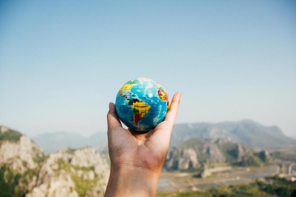 Eine Hand hält einen kleinen Globus vor einer Berglandschaft