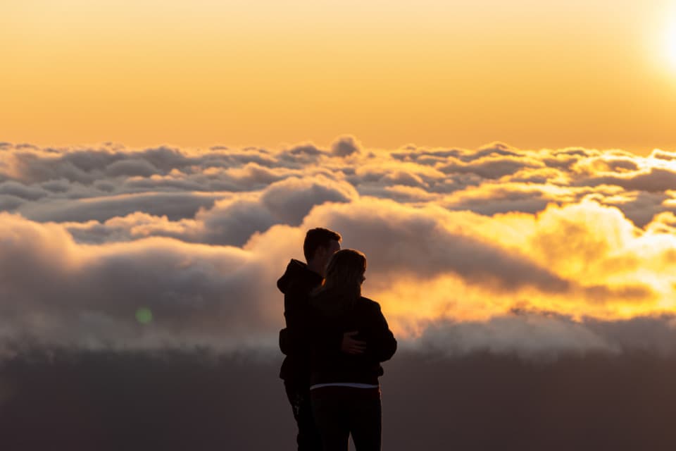 Ein Paar steht umarmt im Gegenlicht über einem Wolkenmeer