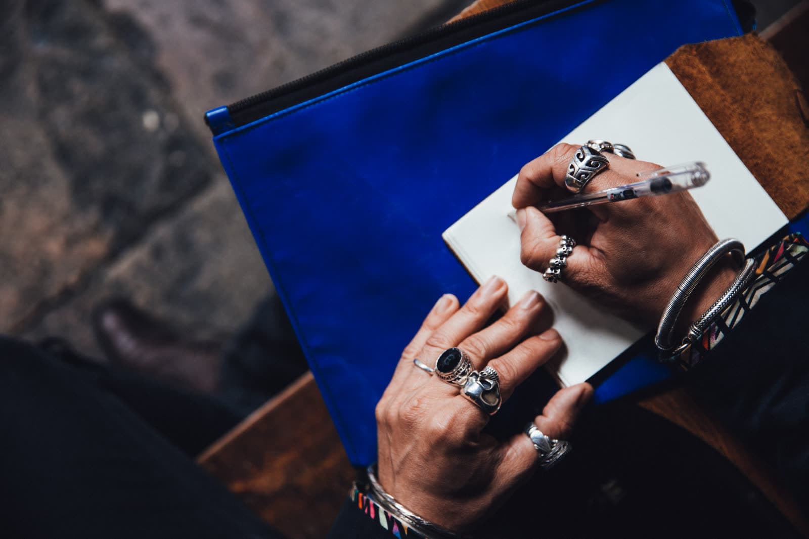 Hand mit Ringen schreibt auf ein Blatt, das auf einer blauen Mappe liegt