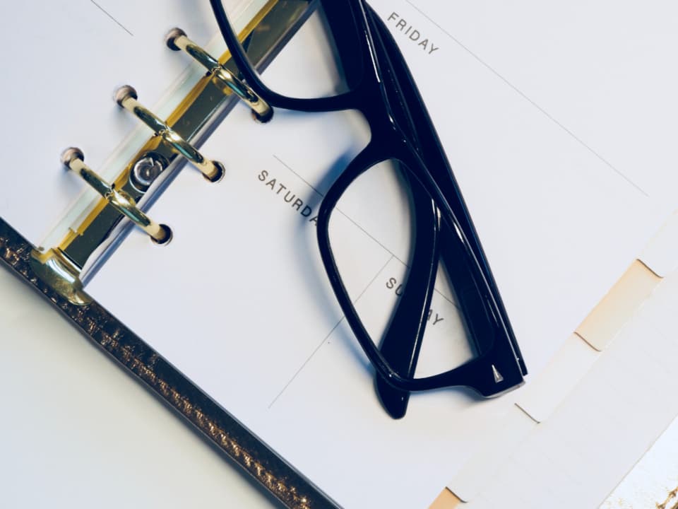 Aufgeschlagener Terminkalender, auf dem eine Brille liegt