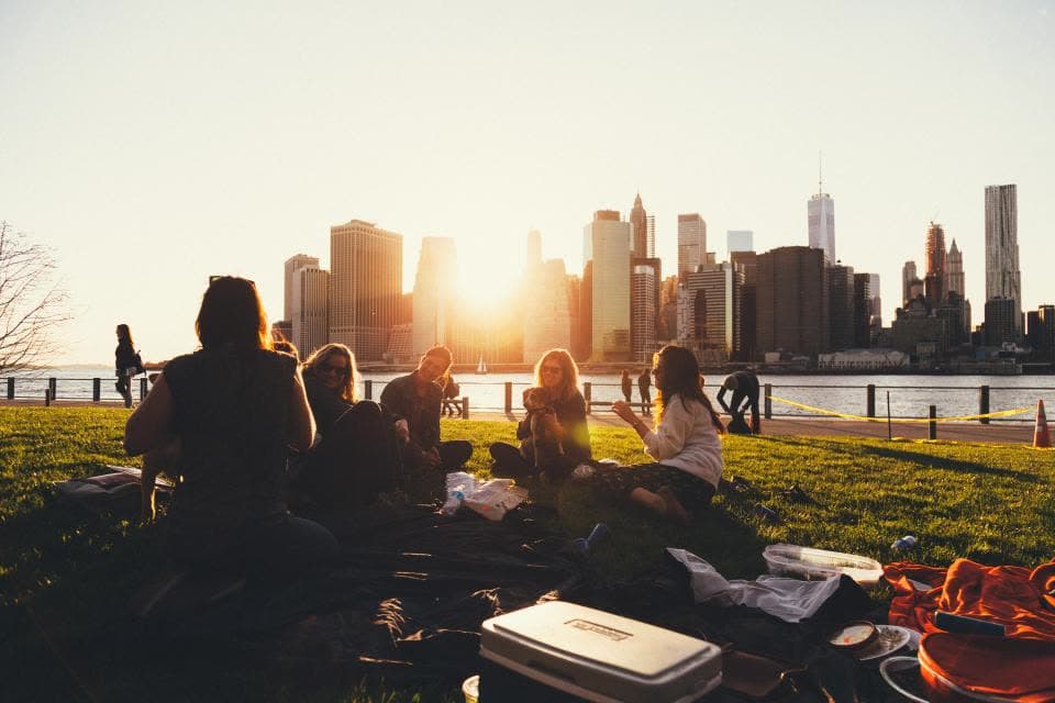 Menschen sitzen bei Sonnenuntergang auf einer Wiese vor einer Stadtsilhouette