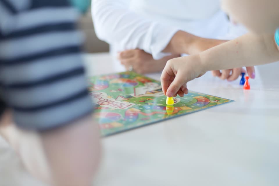 Hand setzt eine Spielfigur auf ein buntes Spielbrett