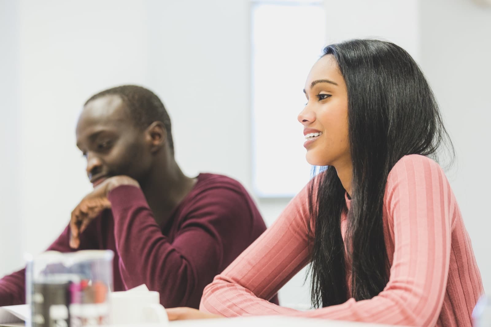 Zwei Studierende sitzen in einem Seminarraum, eine Studentin spricht lächelnd