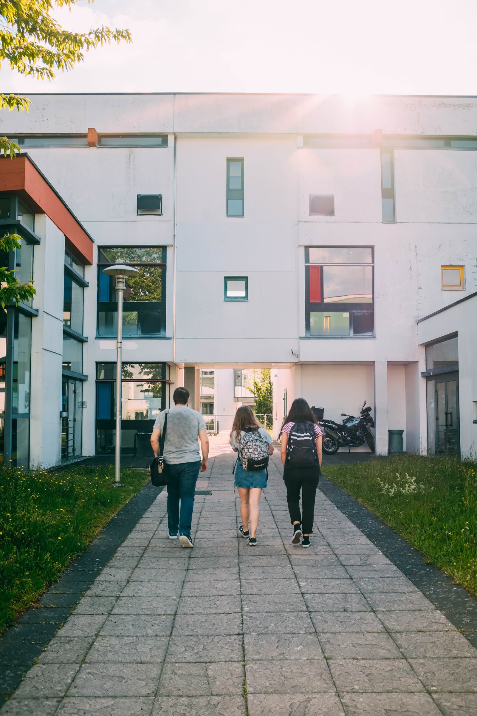 Drei Studierende gehen auf ein Hochschulgebäude zu